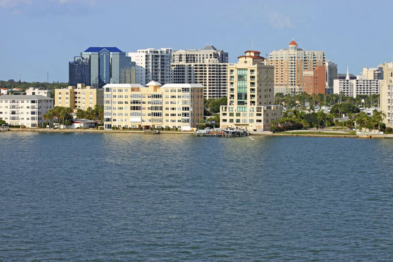 View of buildings on the edge of  Sarasota Bay, Sarasota, Florida from the water with palm trees and a blue sky.