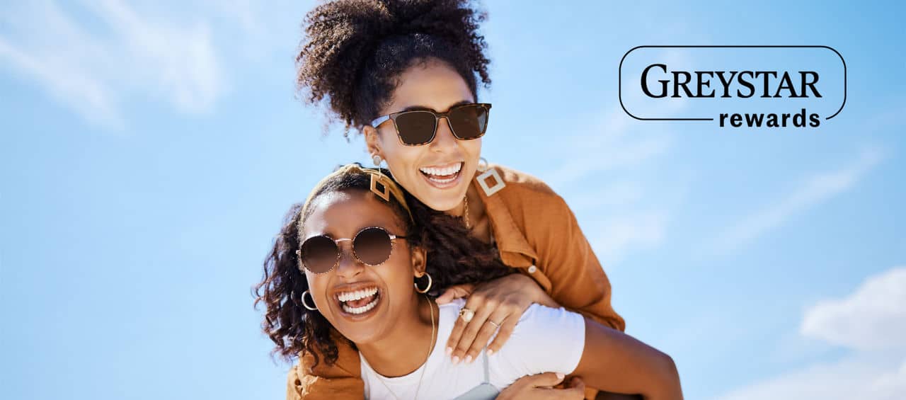 Two women outside, one carrying the other while laughing and smiling with a blue sky in the background and Greystar rewards logo.