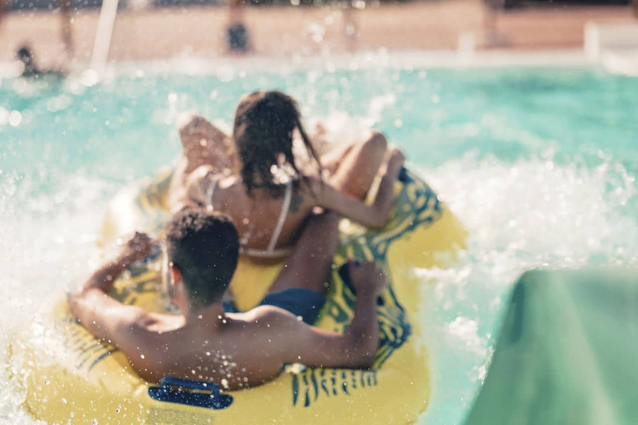 Cool people having fun on the water slide with friends and familiy in the aqua fun park glides playing happy and water splashes are all over. Blue sky background looks amazing sunlight