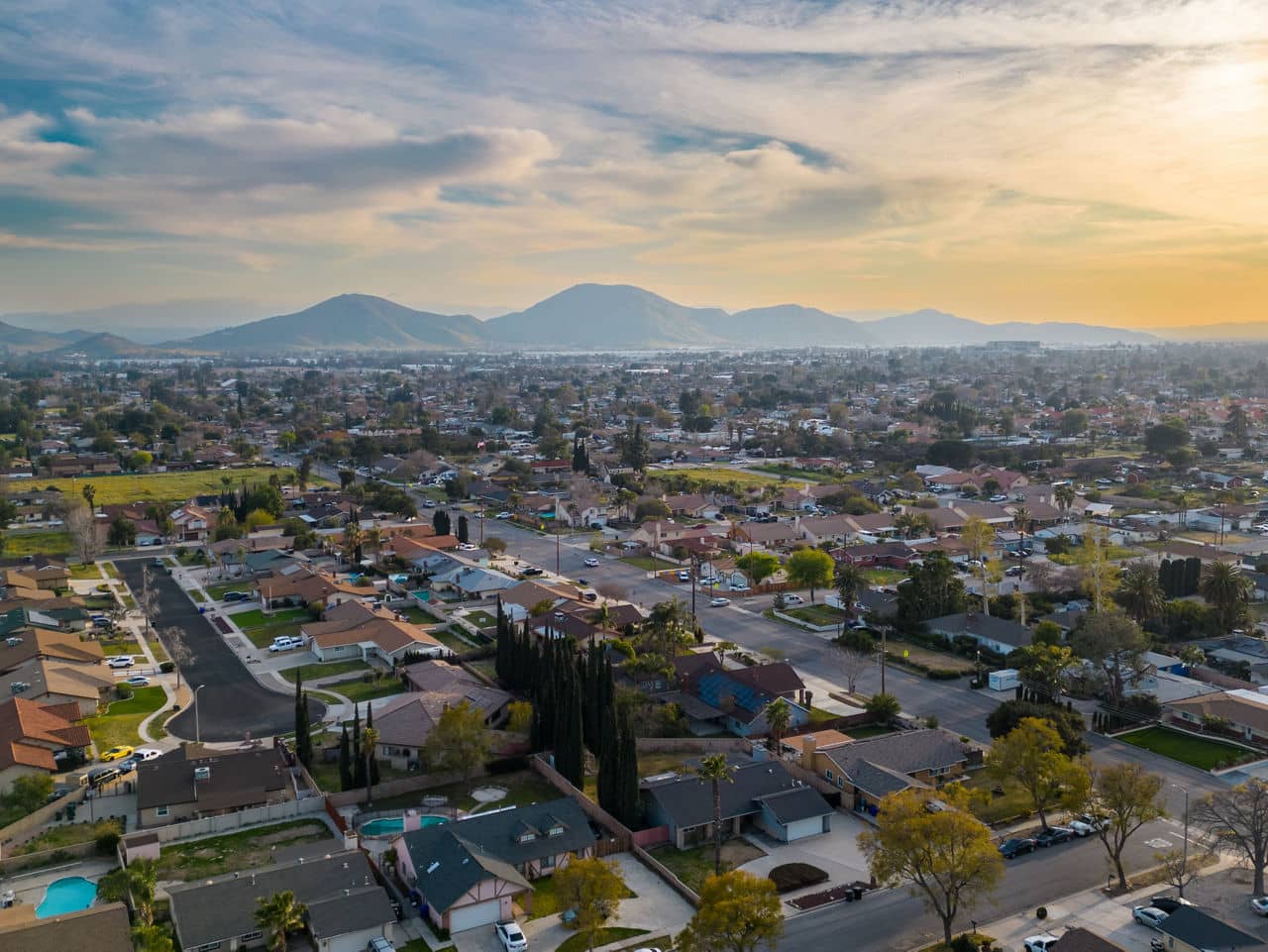A suburban neighborhood in Fontana, California, with rows of houses, tree-lined streets, and mountains in the distance under a sunset sky.