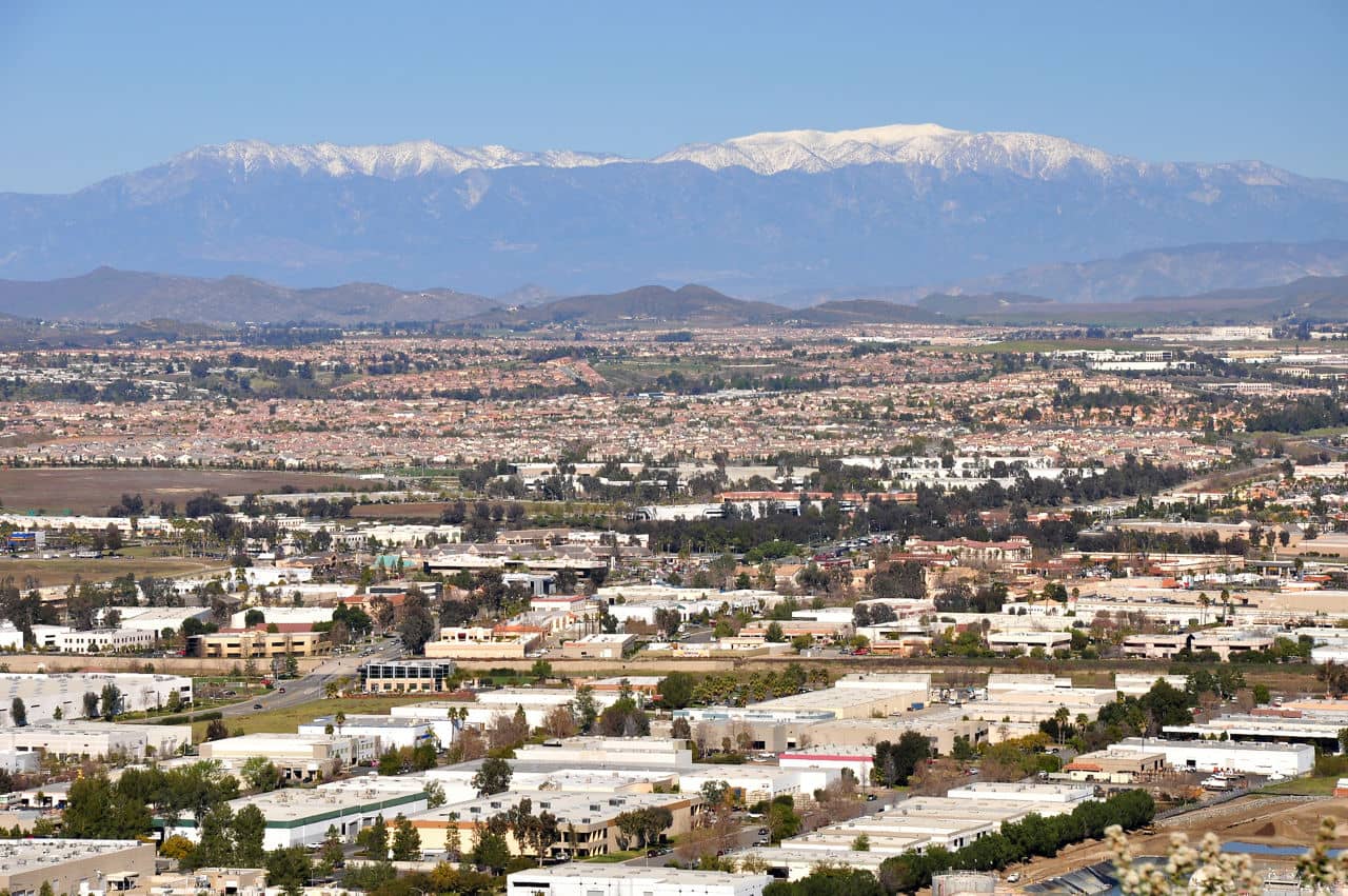 A sprawling view of Murrieta, California, with industrial buildings, residential areas, and snow-capped mountains in the background.