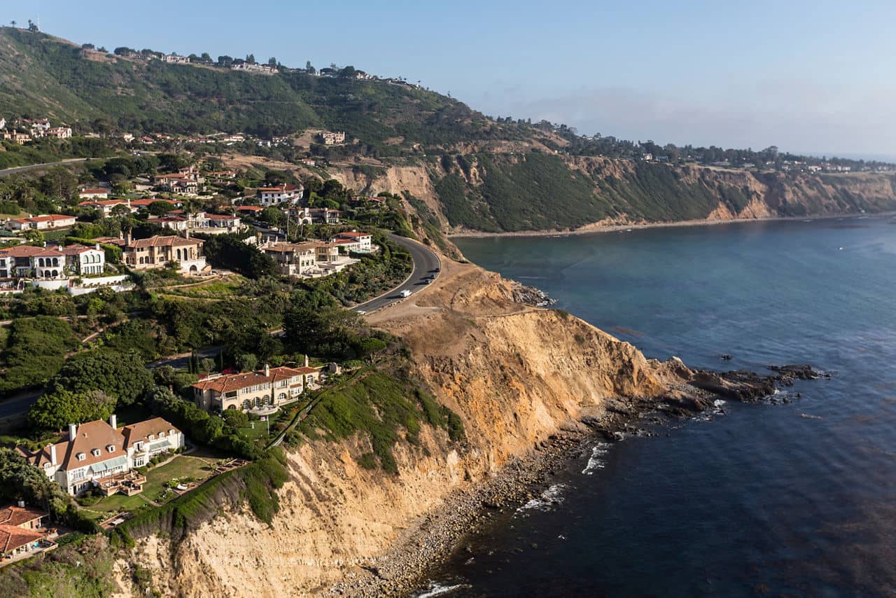 Coastal homes in Culver City, California, overlooking rocky cliffs and the ocean with green hills in the background.