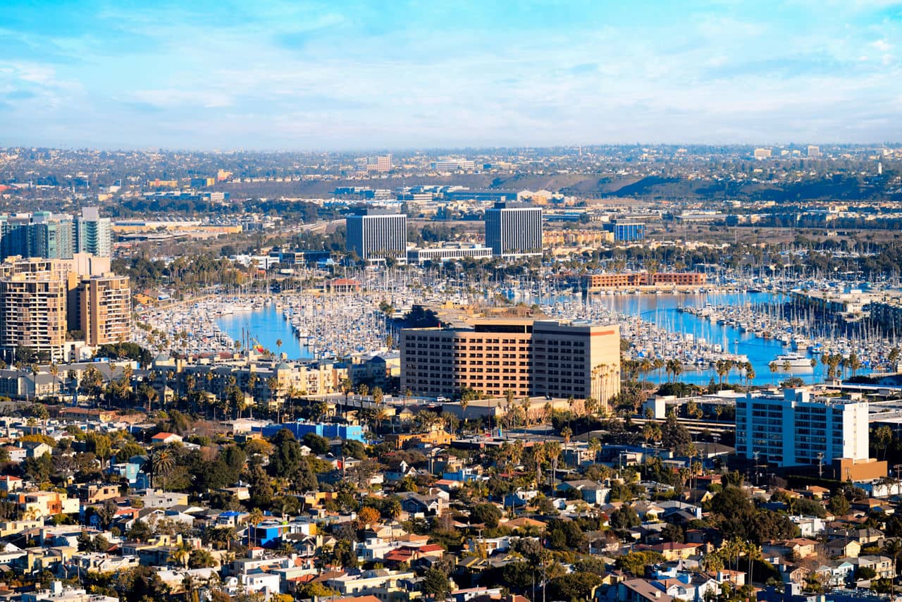 A vibrant marina in Marina Del Rey, California, filled with boats and surrounded by tall buildings and homes under a clear blue sky.