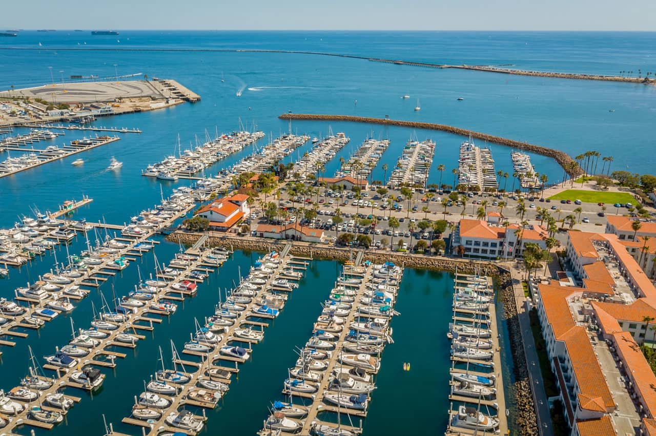 A marina in San Pedro, California, filled with rows of boats and surrounded by buildings with red-tiled roofs along the blue ocean.