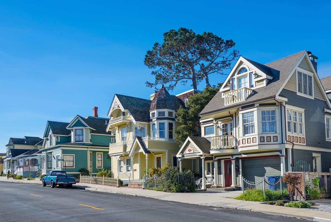 Colorful Victorian-style houses line a quiet street in Monterey, California, under a bright blue sky.