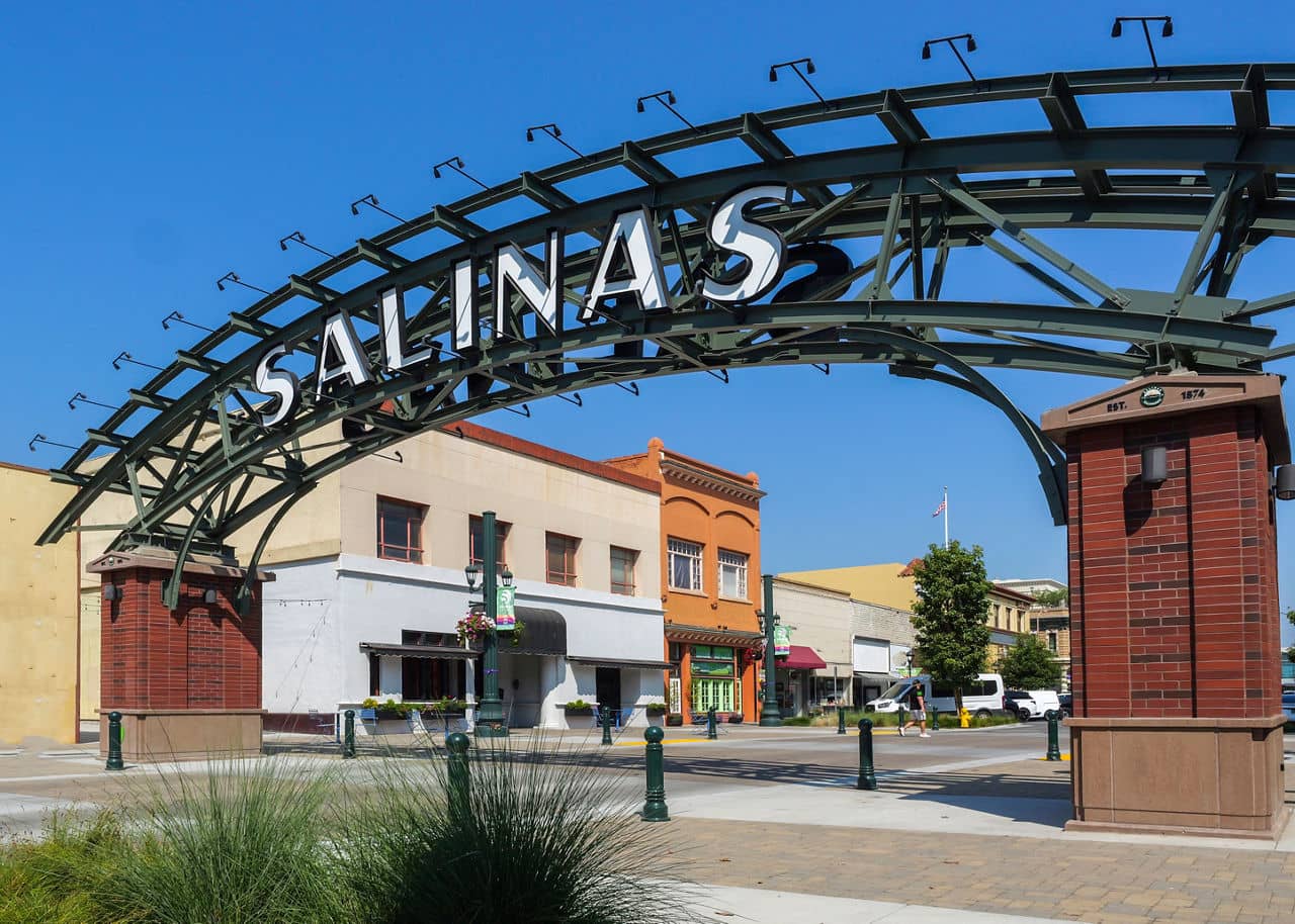 An archway with &quot;Salinas&quot; welcomes visitors to the downtown area in featuring colorful historic buildings under a clear sky.