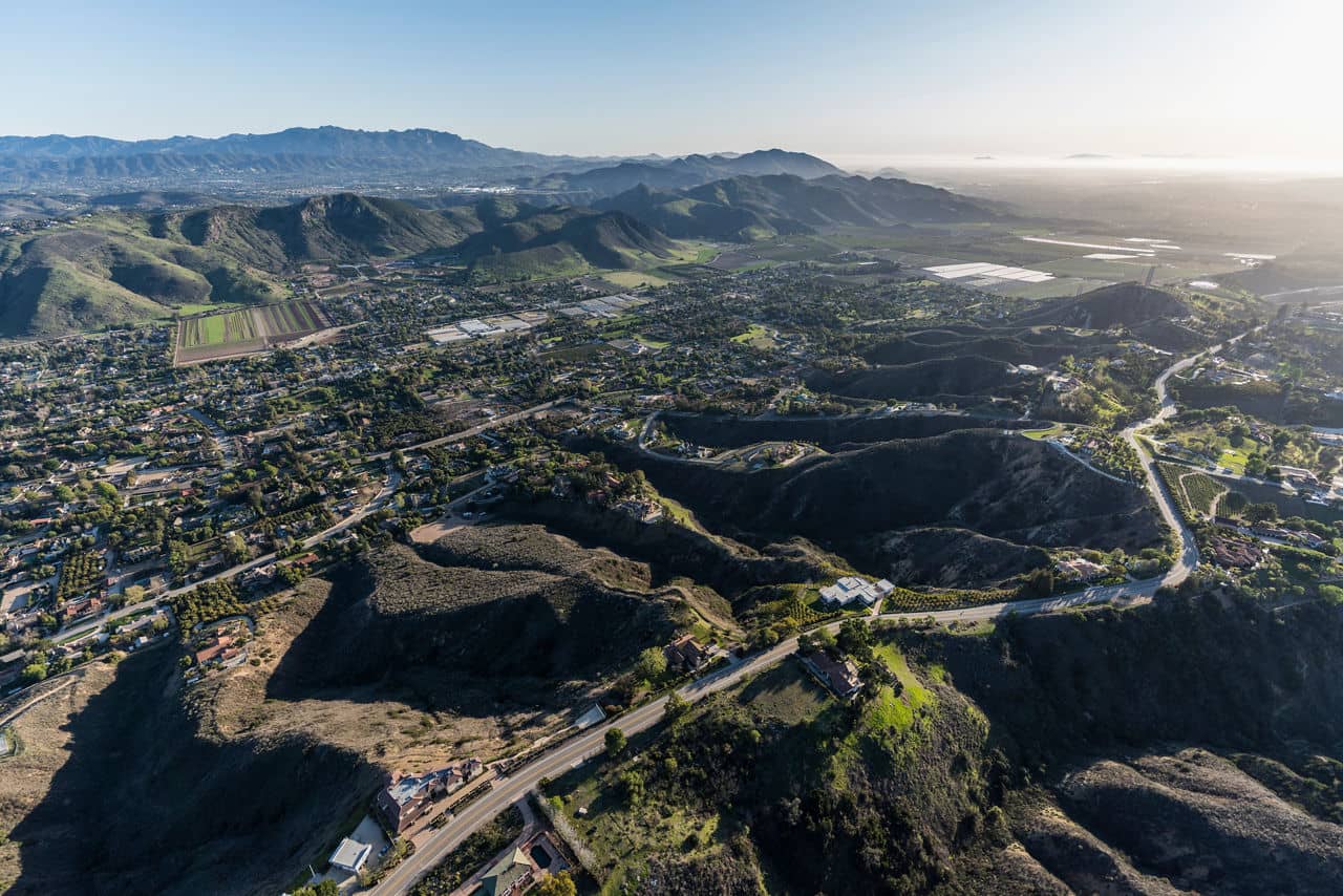 A scenic aerial view of rolling hills and farmlands in Petaluma, California, with scattered homes and distant mountains under a clear sky.