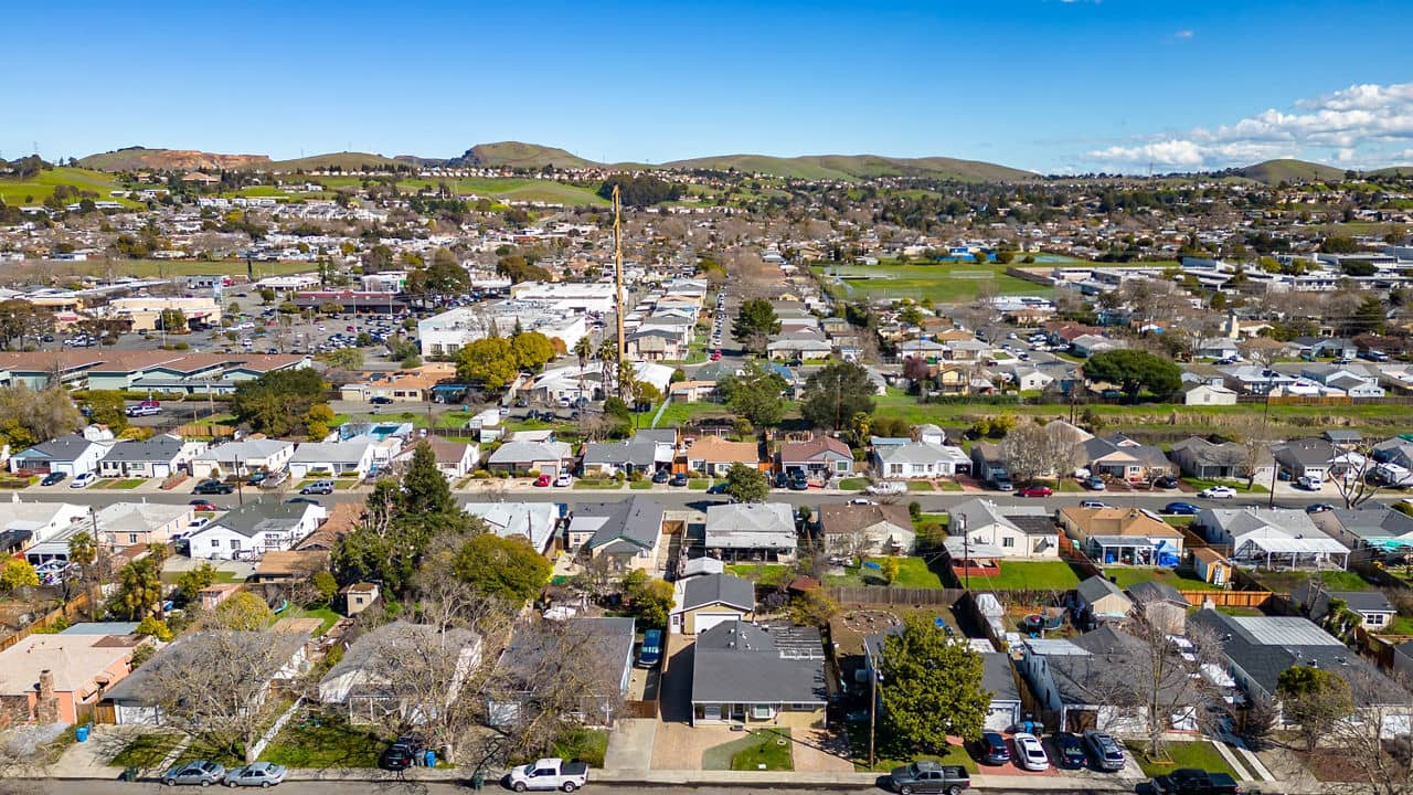 Aerial view of Vallejo, California, showcasing a suburban area with rows of houses, green hills in the background, and a clear blue sky.