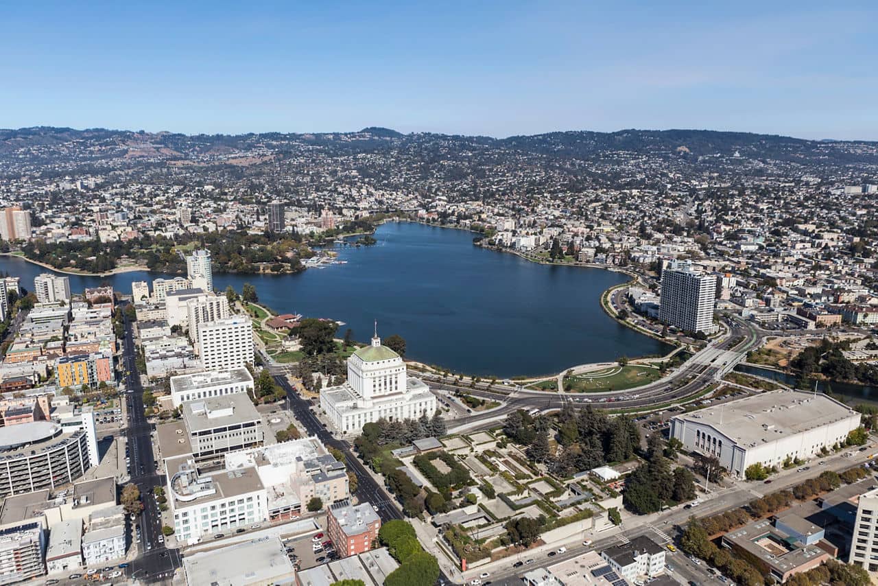Aerial view of Lake Merritt in Oakland&apos;s East Bay, California, showing urban buildings surrounding the lake with hills in the background.