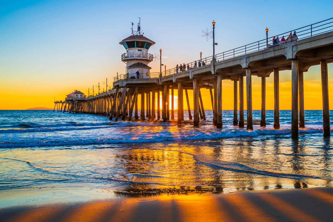 A stunning sunset view at Huntington Beach Pier, California, with golden reflections on the sand and waves under the iconic structure.