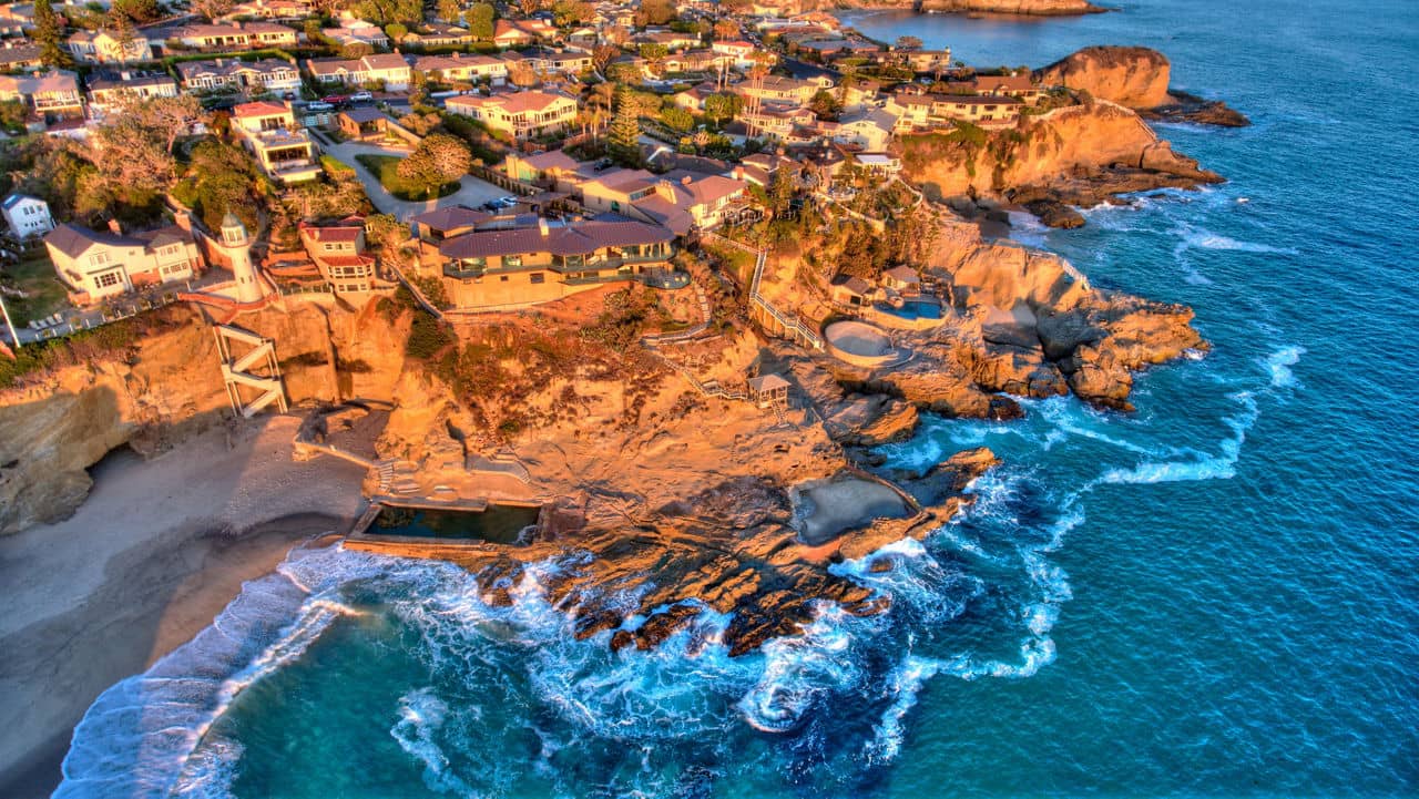 Ariel view of  Laguna Beach, California showcasing the coastal cliffs, waves, and nearby homes.
