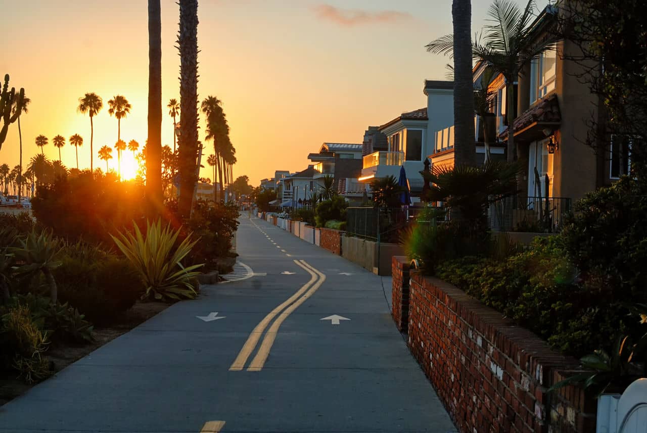 Sunset view in Newport Beach, California, featuring a coastal pathway lined with palm trees, greenery, and upscale homes.