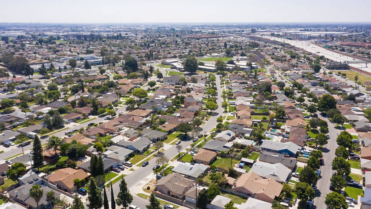 Aerial view of Norwalk, California, showcasing a suburban neighborhood with tree-lined streets, houses, and nearby highways on a clear day.