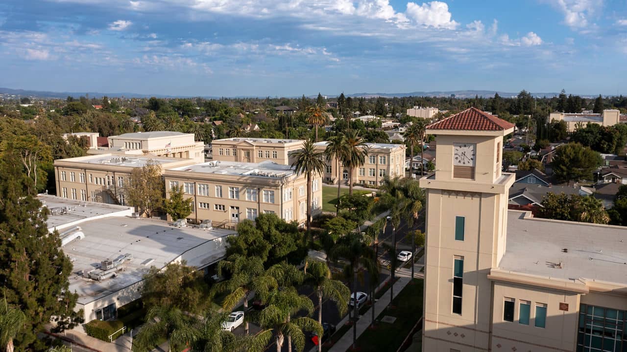 Aerial view of Orange, California, showcasing historic beige buildings, palm trees, and a clock tower under a partly cloudy sky.