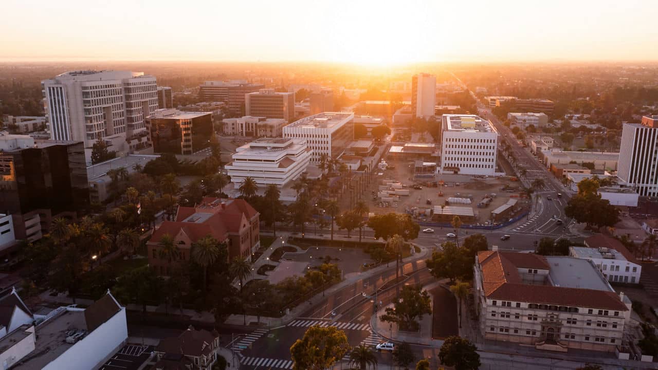 An aerial view of Santa Ana/Tustin, California, at sunset, showing city buildings, palm trees, and streets bathed in warm light.