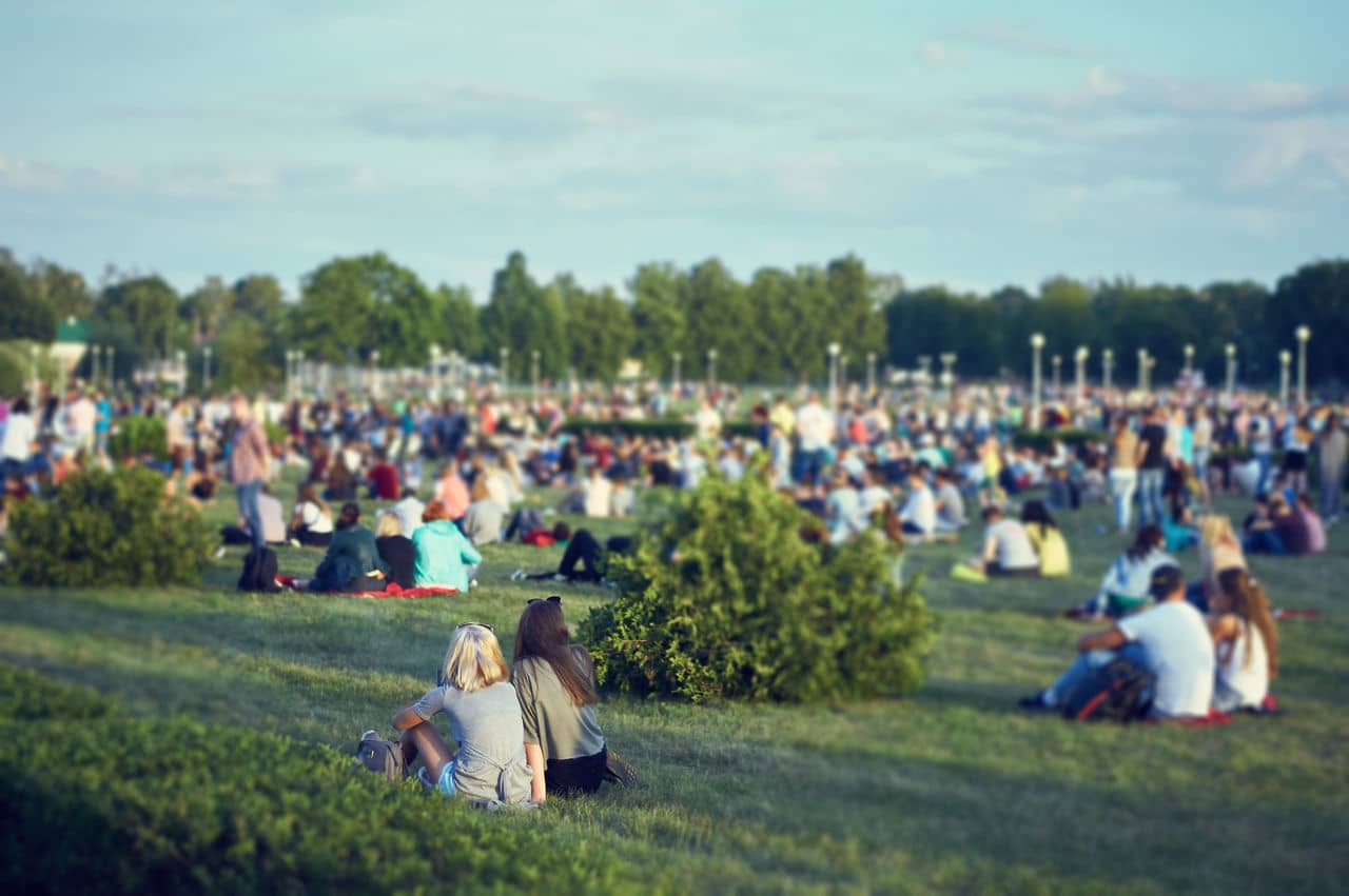 Large crowd relaxing on grassy hillside at outdoor event in Carmichael, California, with trees and lamp posts in background.