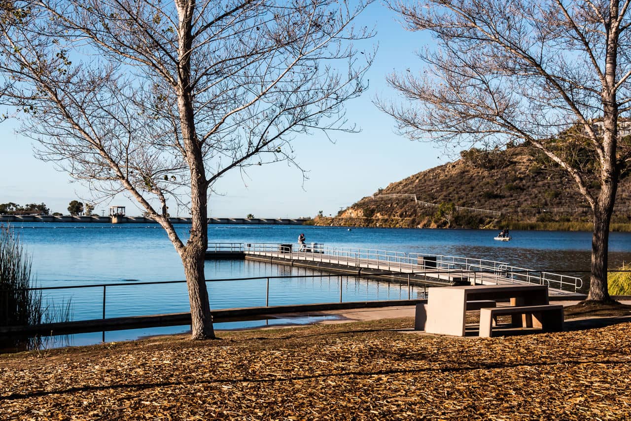 Peaceful lakeside view in Grantville, California, showing a wooden dock, calm water, dry trees, and a picnic table in the foreground.