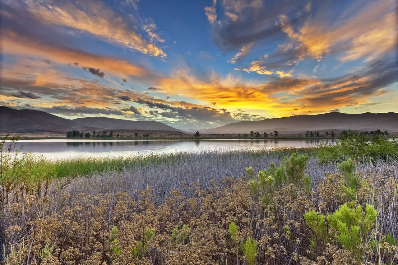 Scenic view of a serene lake at sunset with colorful skies, mountains, and lush vegetation in Otay Ranch, California.