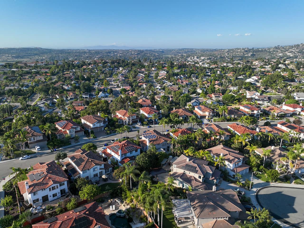 Aerial view of Vista, California, showing Spanish-style homes with red tile roofs, palm trees, and solar panels spread across hills.