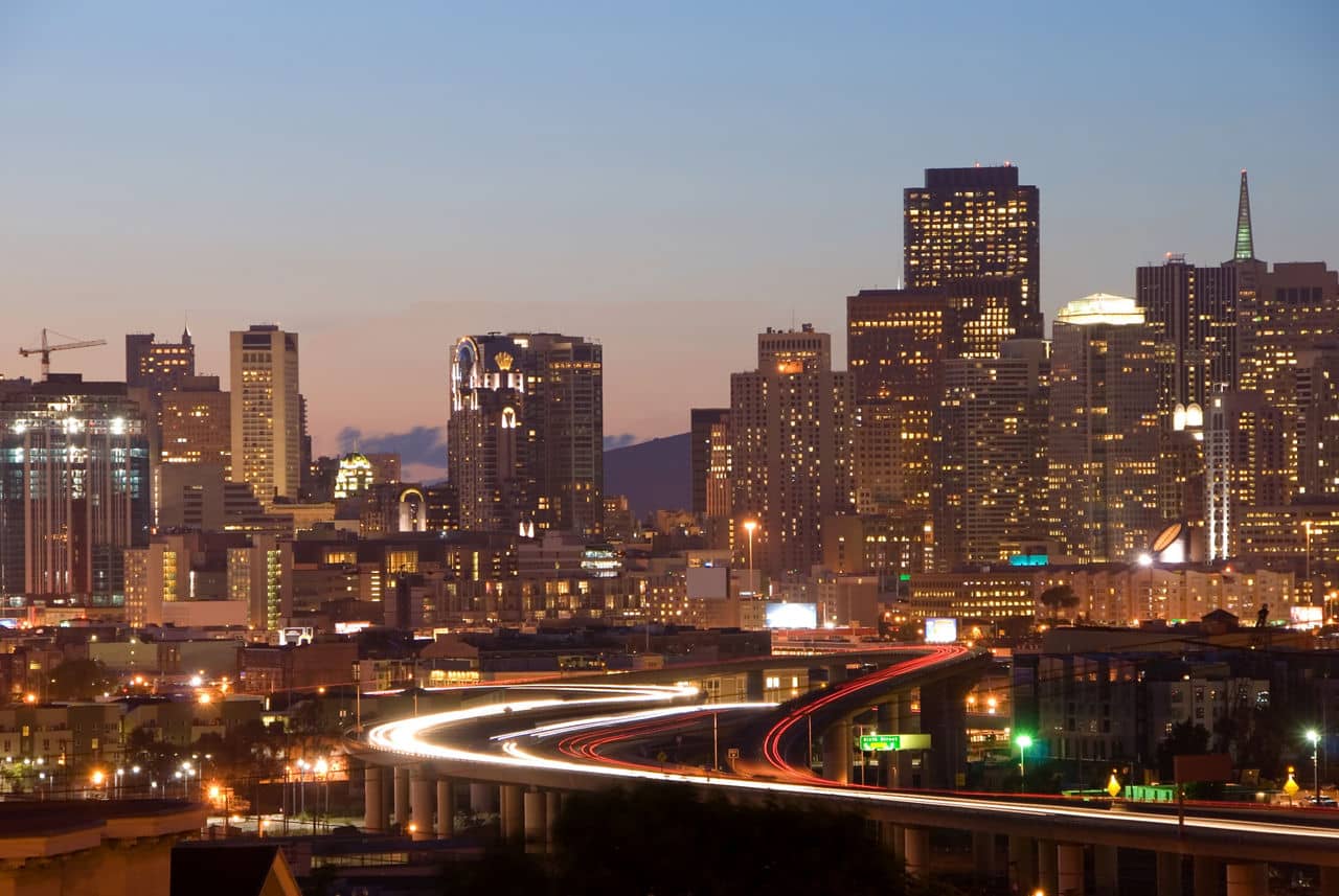 View from Potrero Hill, California, showing lit city skyline at dusk with glowing car trails on curved highway below.