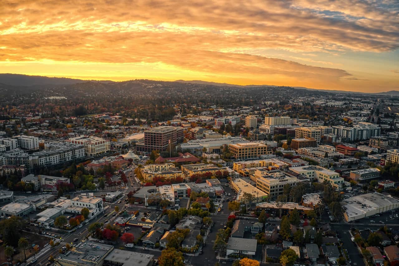 Sunset aerial view of downtown Redwood City, California, with golden clouds above and fall-colored trees scattered throughout the city.