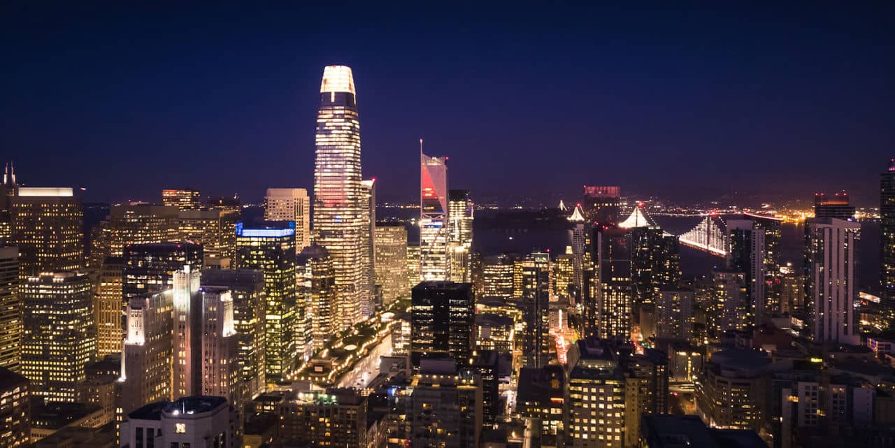Night view of South of Market, California, with Salesforce Tower glowing bright and Bay Bridge lights in the distance.