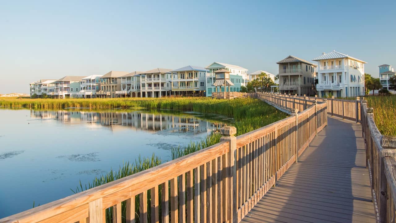Wooden boardwalk over marshland in the Destin Area, Florida, leading to pastel-colored beach houses built on stilts.