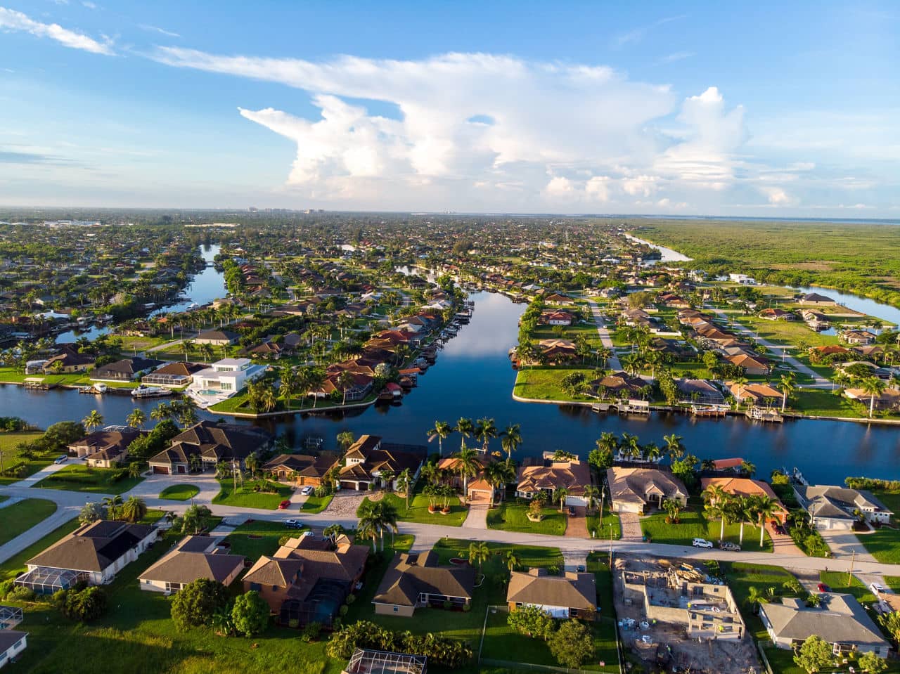 Aerial view of Fort Myers/Cape Coral, Florida, with homes along winding canals, palm trees, and natural wetlands in the distance.