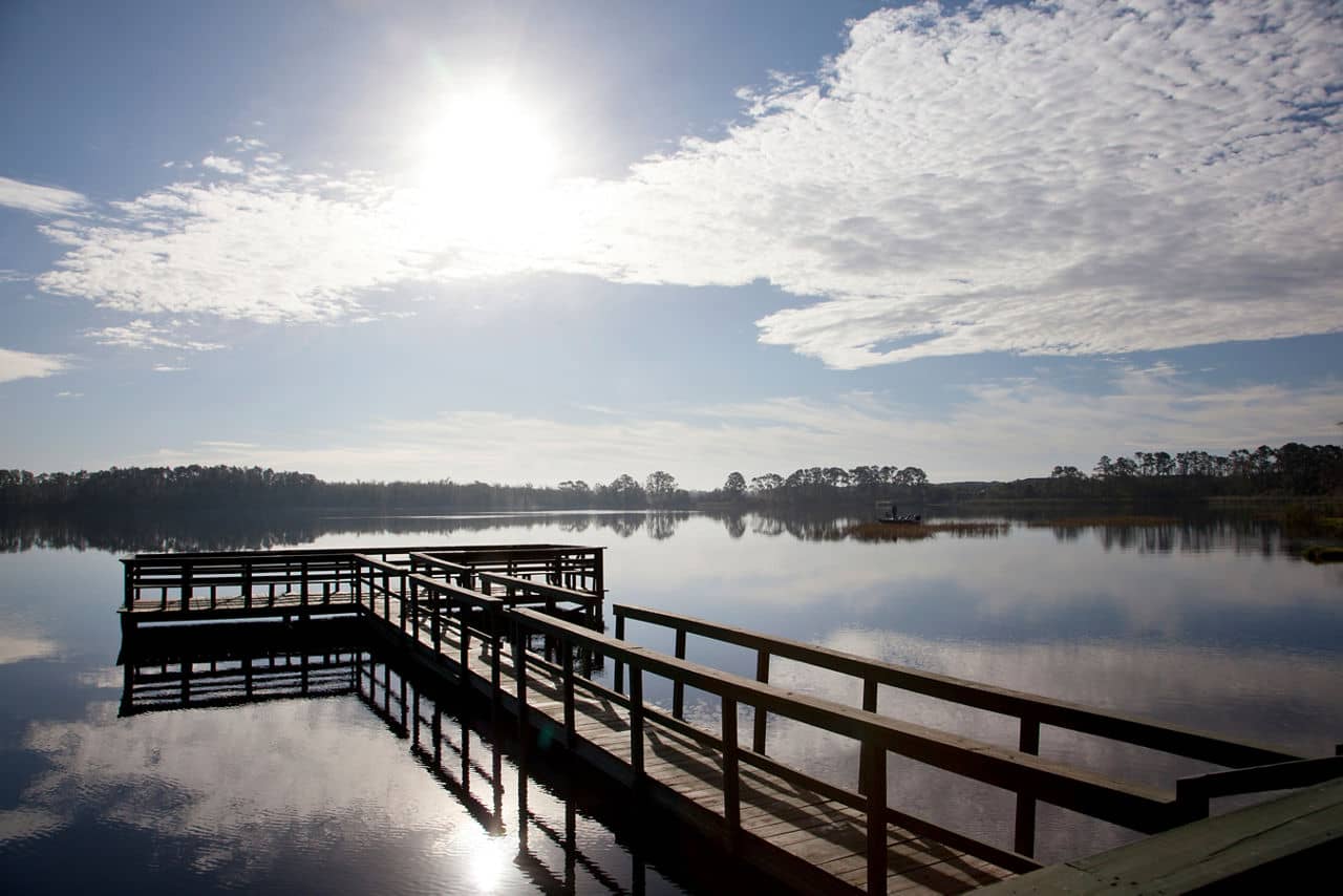 Wooden fishing pier extends over a serene lake in Davenport, Florida, with morning sun reflecting on still waters.