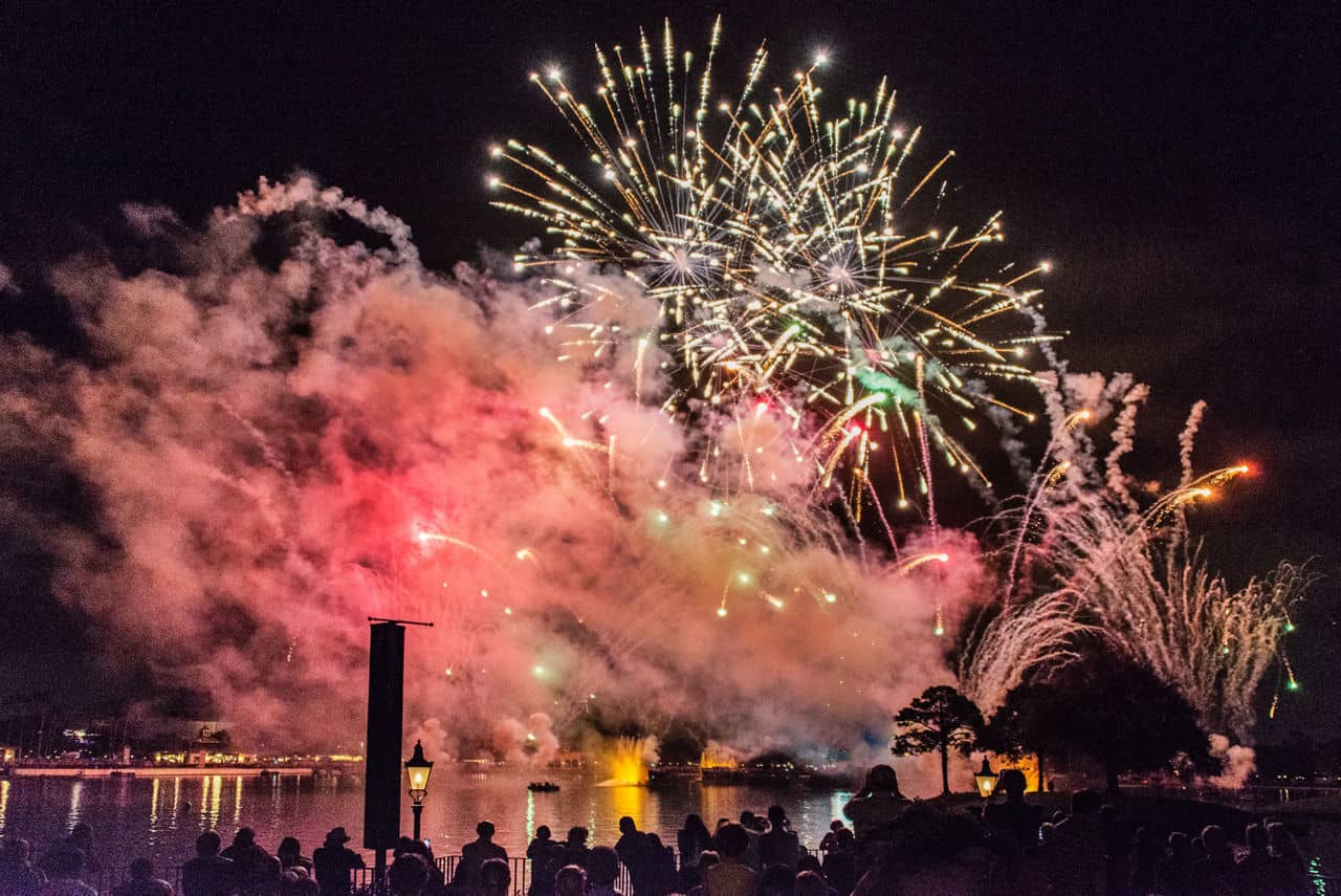  Colorful fireworks display over a lake in Disney Area, Florida, with silhouettes of crowd watching from waterfront.