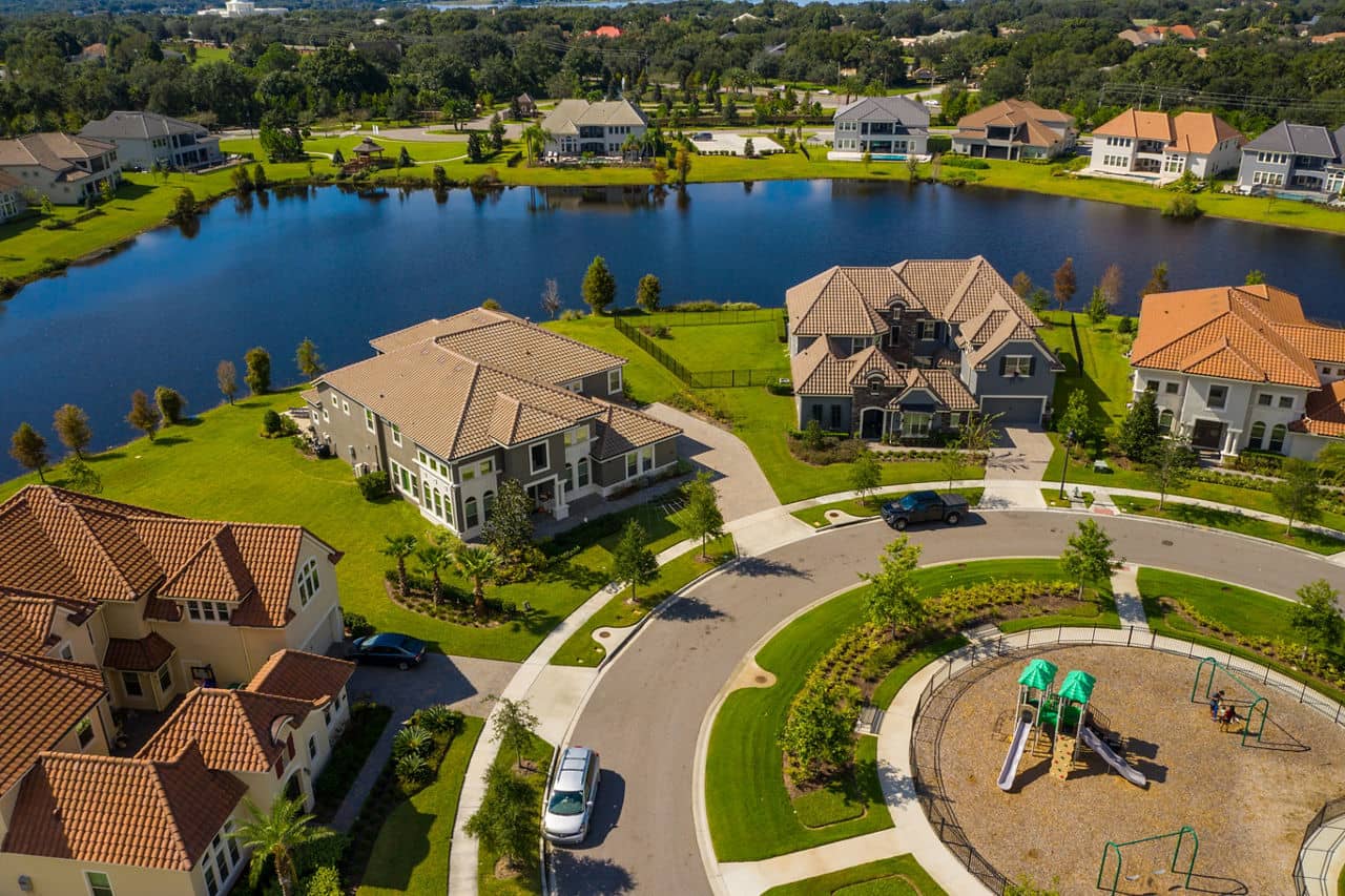 Aerial view of Four Corners, Florida, showing luxury lakefront homes with tile roofs, curved streets, and a playground.
