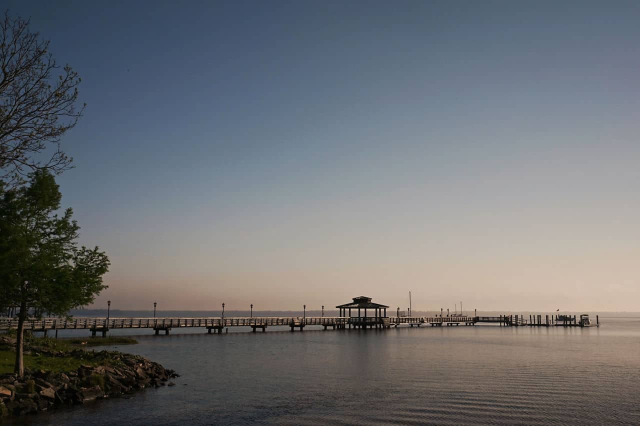  Long wooden fishing pier with gazebo at St Cloud, Florida, extending over calm water at dawn or dusk with clear sky.