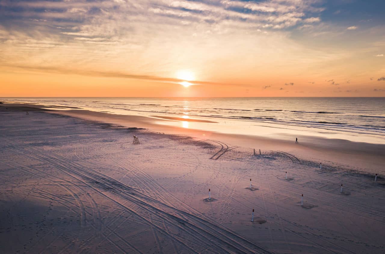 The sunset over a wide sandy beach with tire tracks in Wildwood, Florida