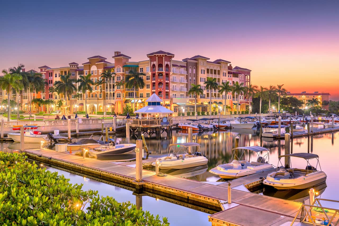 Sunset view of a marina in Naples, Florida with palm tress and multicolored buildings in the background