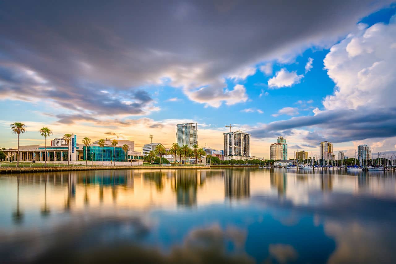 St. Petersburg, Florida waterfront at sunset with modern buildings, palm trees, and marina perfectly reflected in still water.