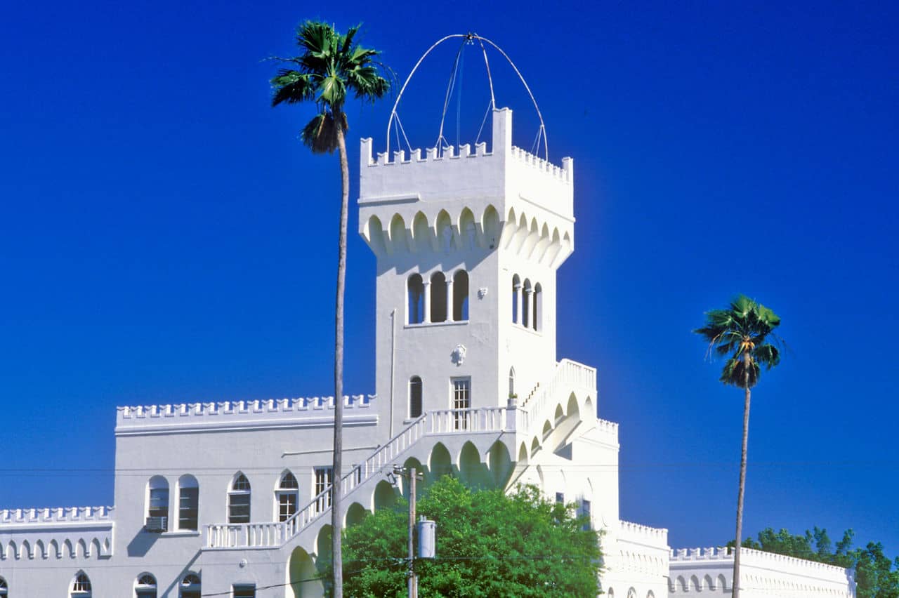 White castle-like building with arches and tower in Hyde Park, Florida, framed by palm trees against bright blue sky.