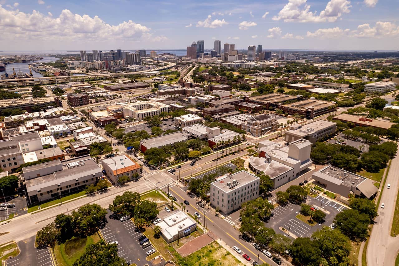 Aerial view of Ybor City, Florida, with historic low-rise buildings in foreground and Tampa&apos;s downtown skyline and bay in the distance.