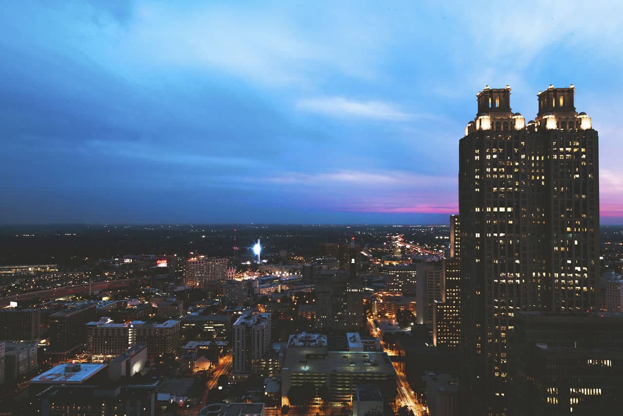 Evening view of Brookhaven, GA with illuminated skyscrapers against dusk sky and city lights stretching to the horizon.