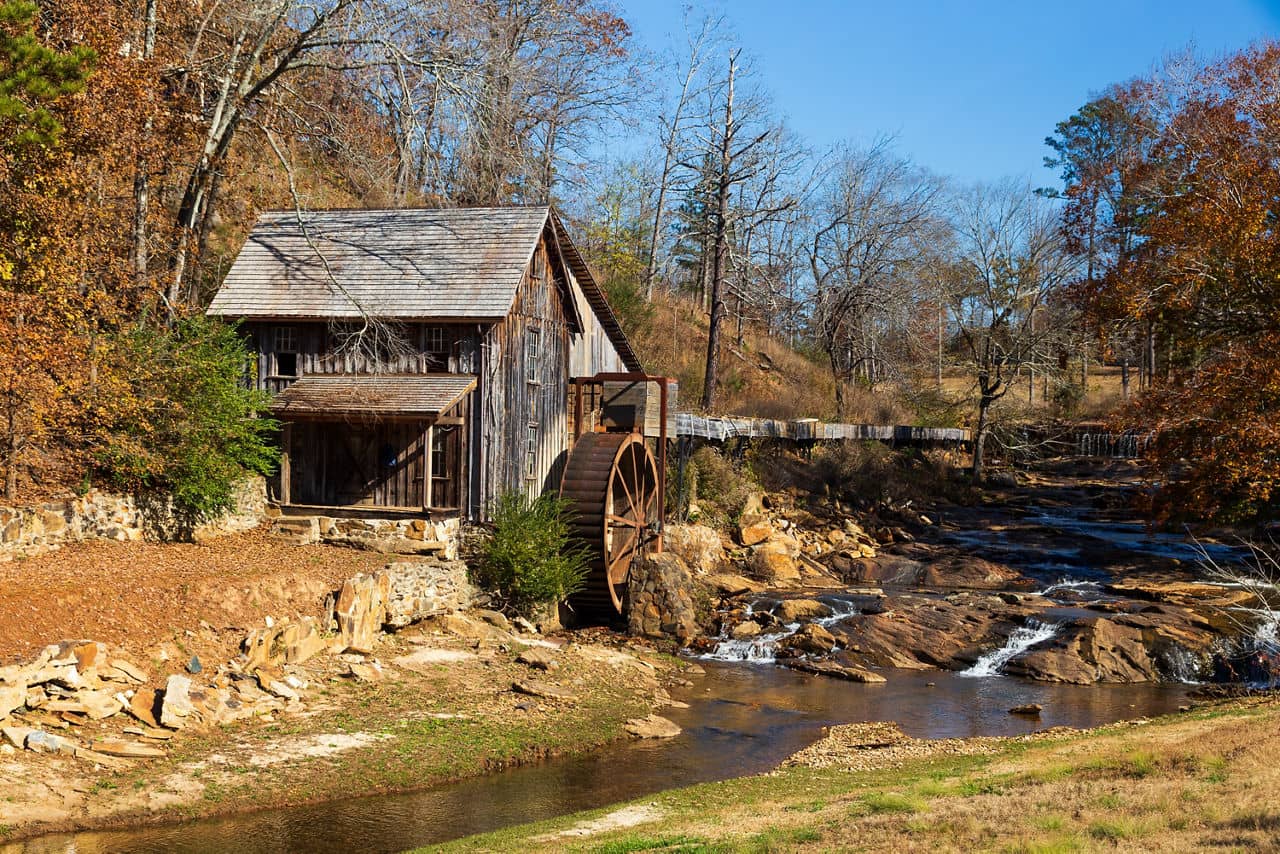 Historic wooden grist mill with water wheel in Cherokee County/Bartow County, GA surrounded by autumn trees and a creek.