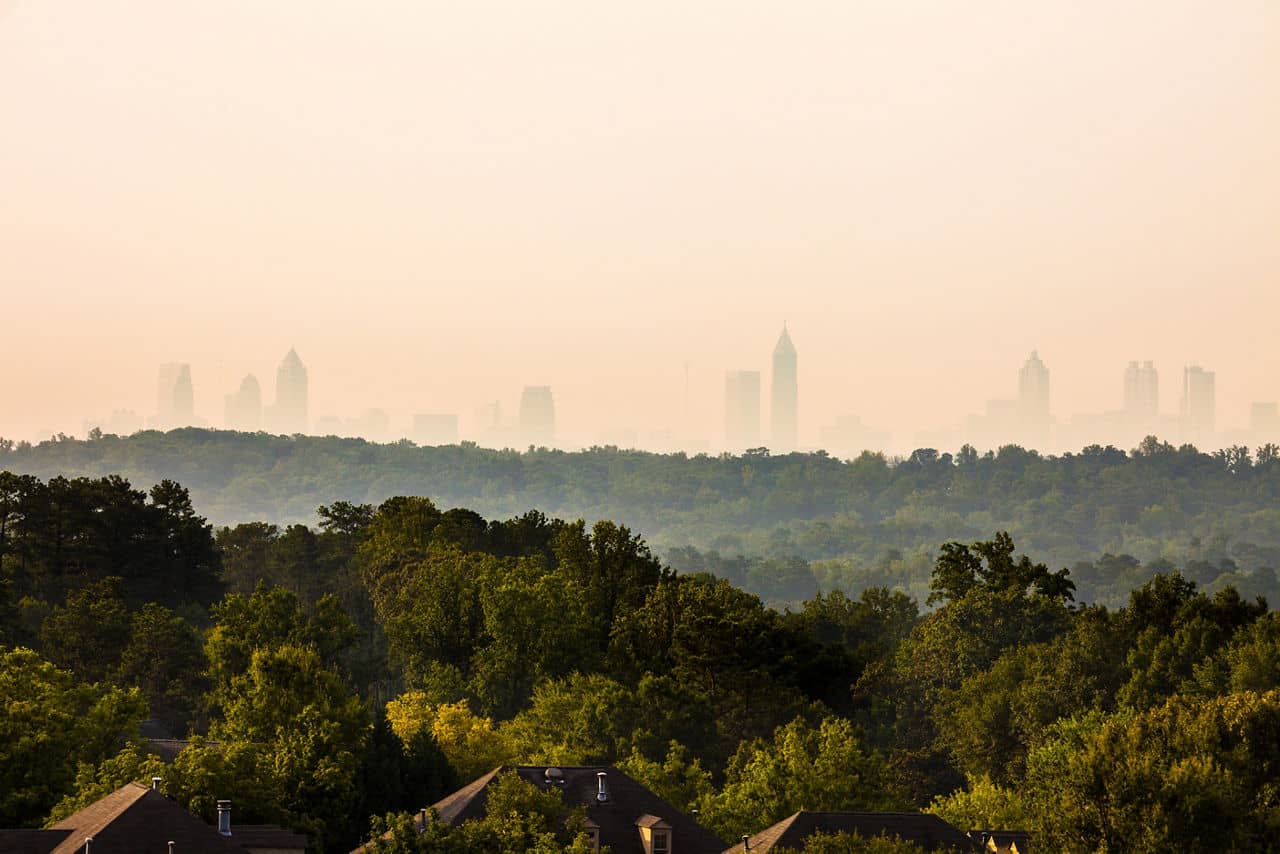 Misty morning view from Cobb County, GA with dense green forest and Atlanta skyline silhouette visible in the distance.