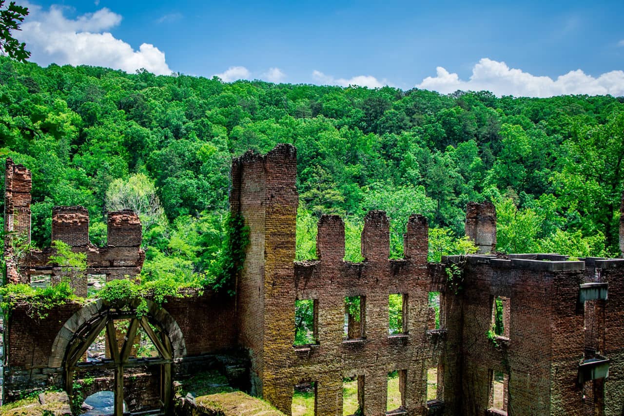 Historic brick ruins of an old mill or factory in Douglas County/Carroll County, GA surrounded by lush green forest.