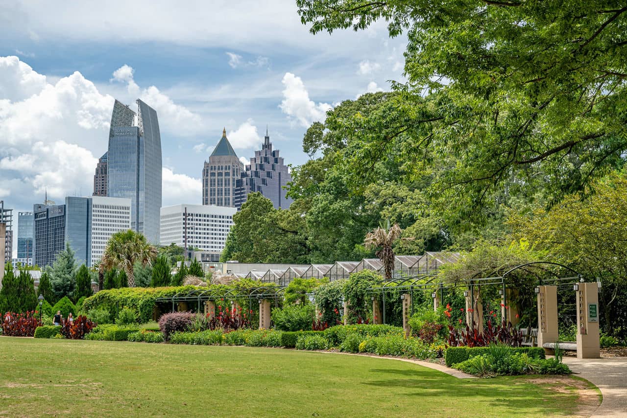 Lush garden in Villa Rica, GA with flower-covered pergola, lush lawn, and Atlanta skyline in the background under a blue sky.