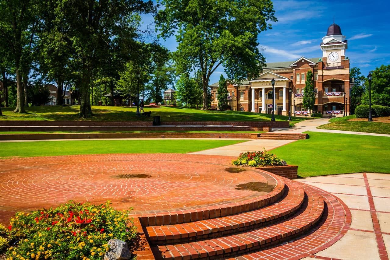 Brick plaza leading to Duluth, GA city hall with clock tower, American flag decor, and landscaped grounds with shade trees.