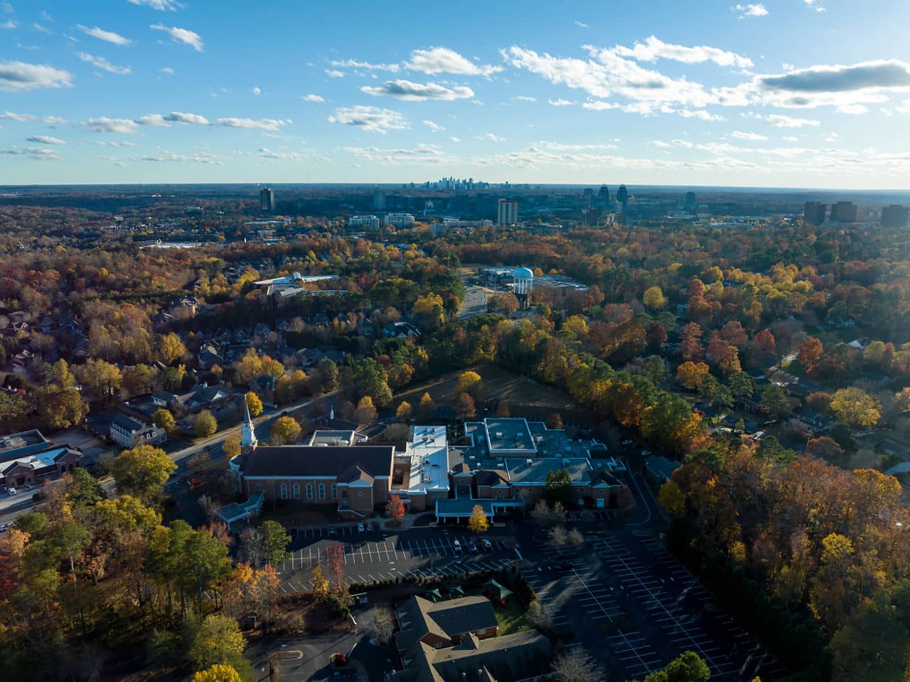 View of Newnan, GA with a large church, autumn trees surrounding neighborhoods, and the Atlanta skyline in the distance.
