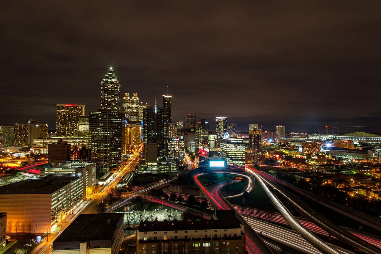 Night skyline view from Smyrna/Vinings, GA with illuminated Atlanta skyscrapers, highway lights, and sports venues.