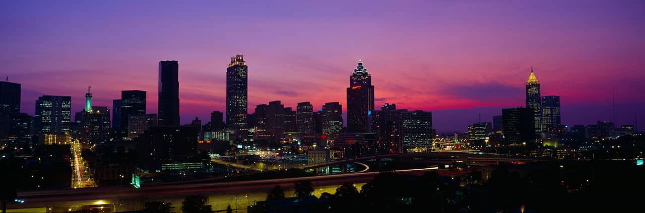 City skyline of Atlanta at sunset viewed from South Fulton County, GA, with purple and pink sky and illuminated skyscrapers.