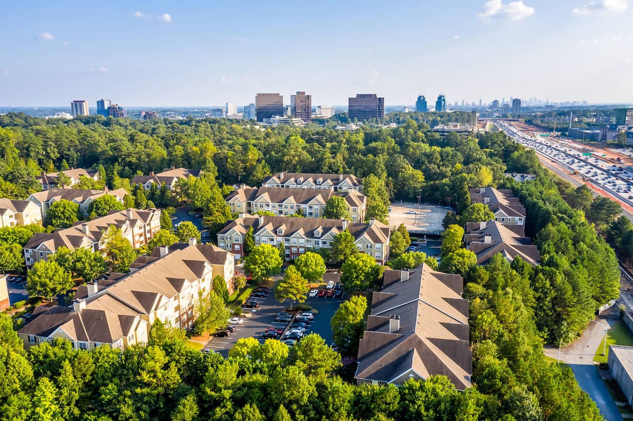 Aerial view of South Fulton, Georgia, showing apartments surrounded by trees with a city skyline and a highway.
