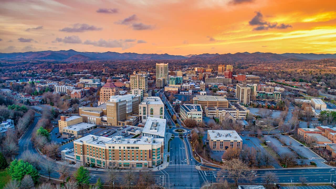 Aerial sunset view of downtown Asheville NC with mountain backdrop and residential communities - North Carolina mountain living