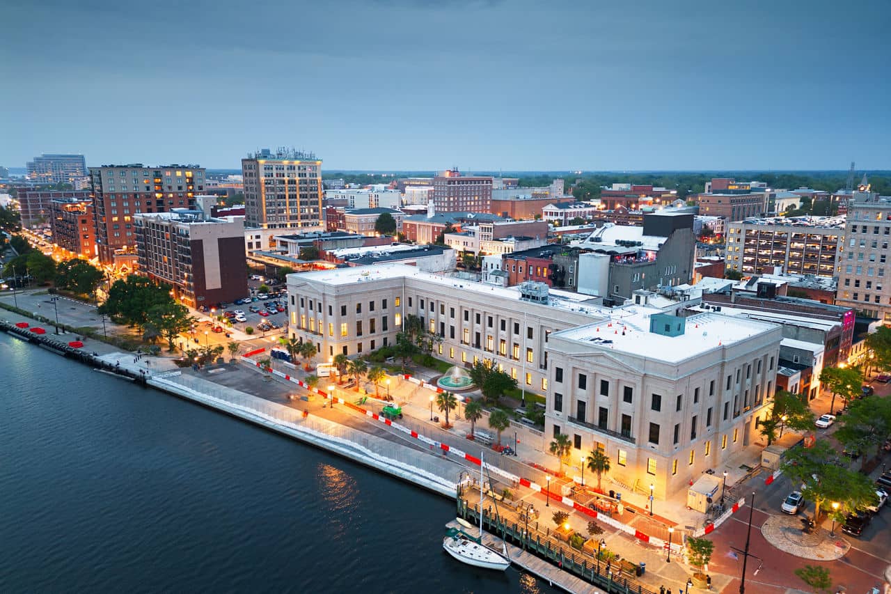 Aerial cityscape and downtown skyline of Wilmington, North Carolina, reflected in the Cape Fear River at sunset.