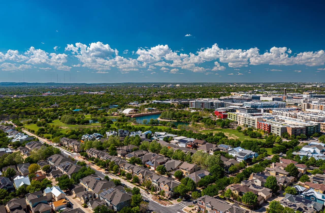Aerial view of the Mueller/East MLK neighborhood in Texas, showing green parks, houses, and modern buildings under a blue sky.